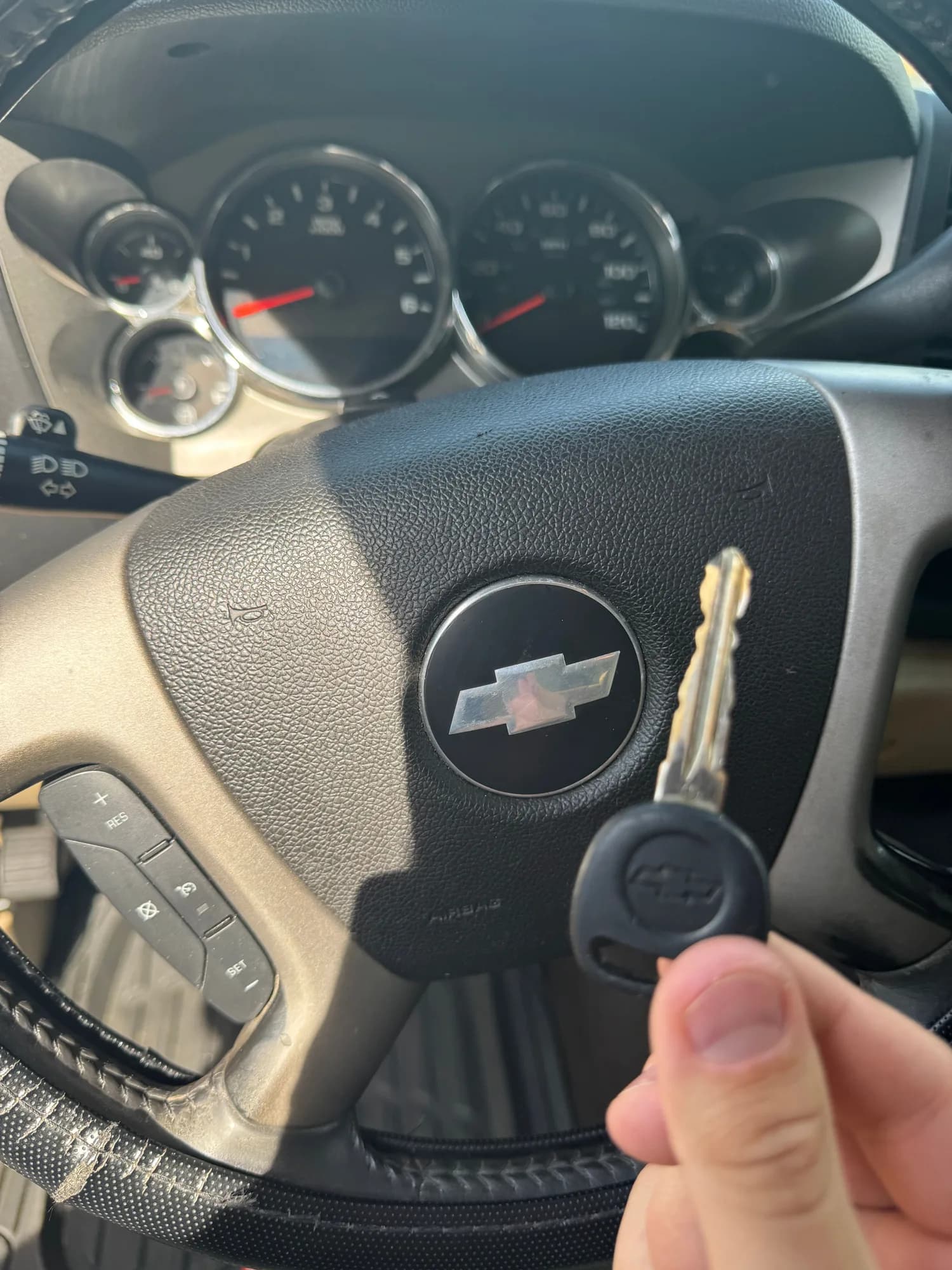 A hand holding a Chevrolet transponder key in front of the steering wheel and instrument cluster of the truck it was cut for