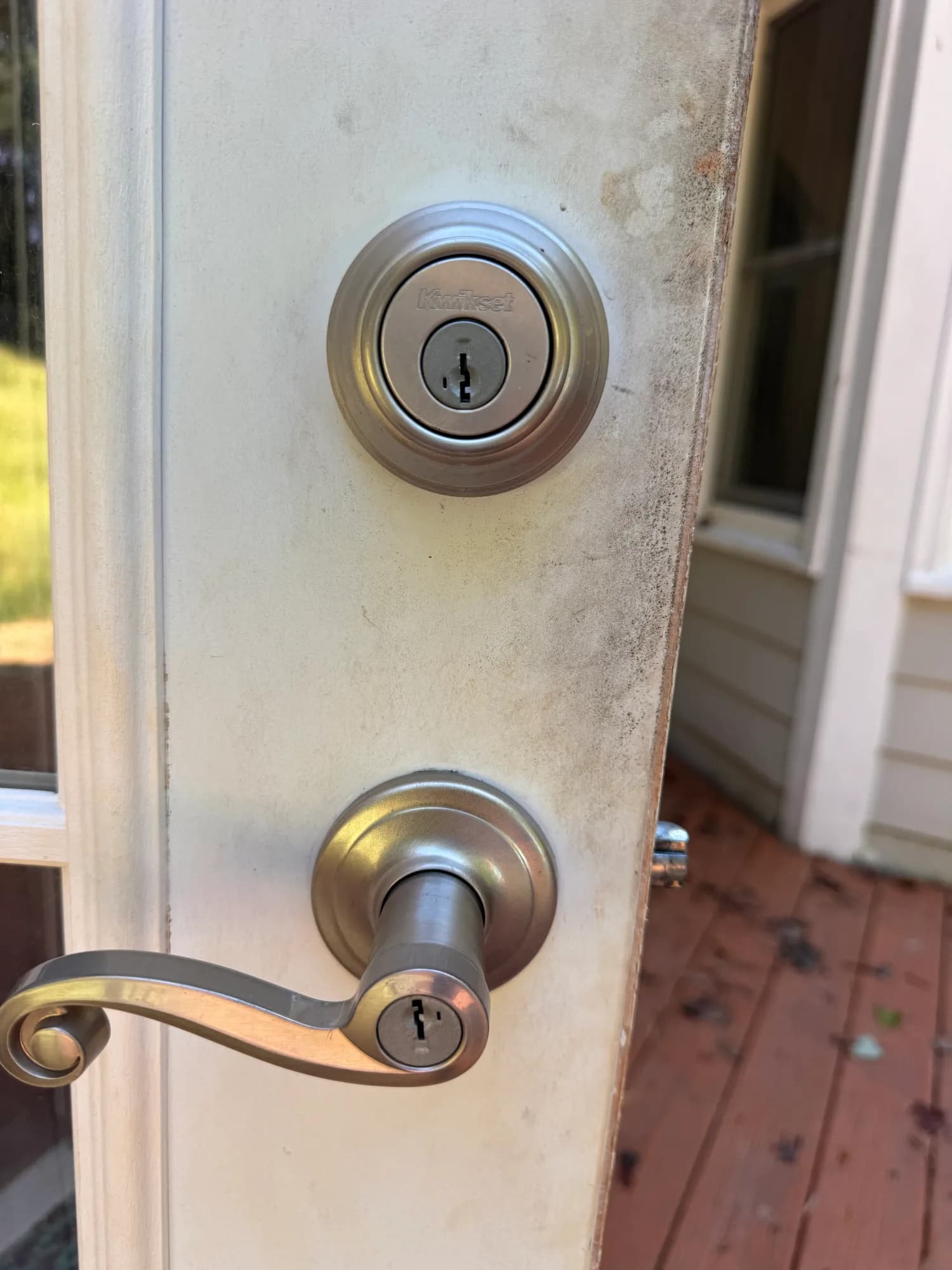 A Kwikset deadbolt and lever handle on a weathered exterior door beside a porch window