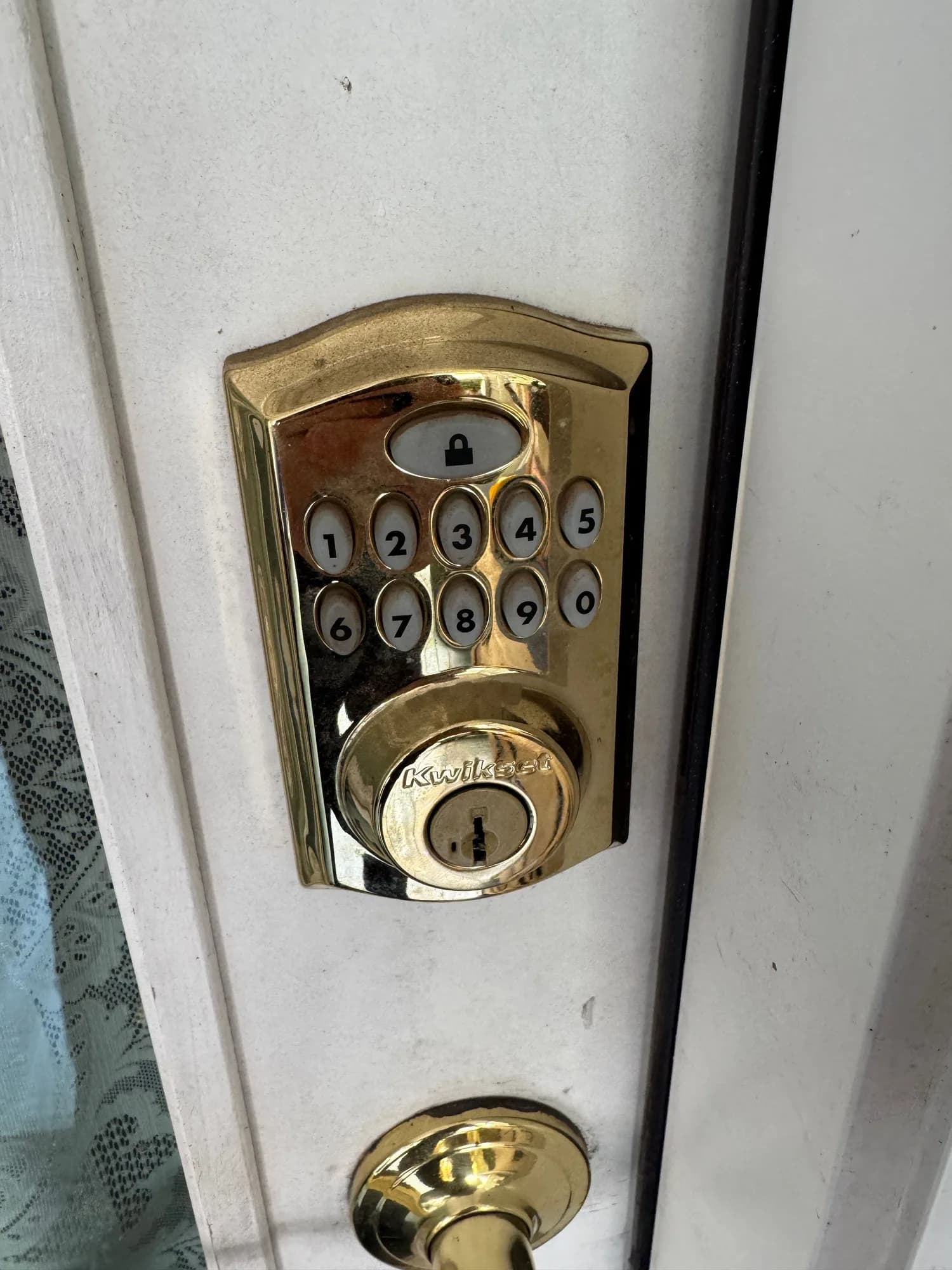 A brass Kwikset keypad deadbolt on a white front door, with a numbered keypad above and a keyed cylinder below it
